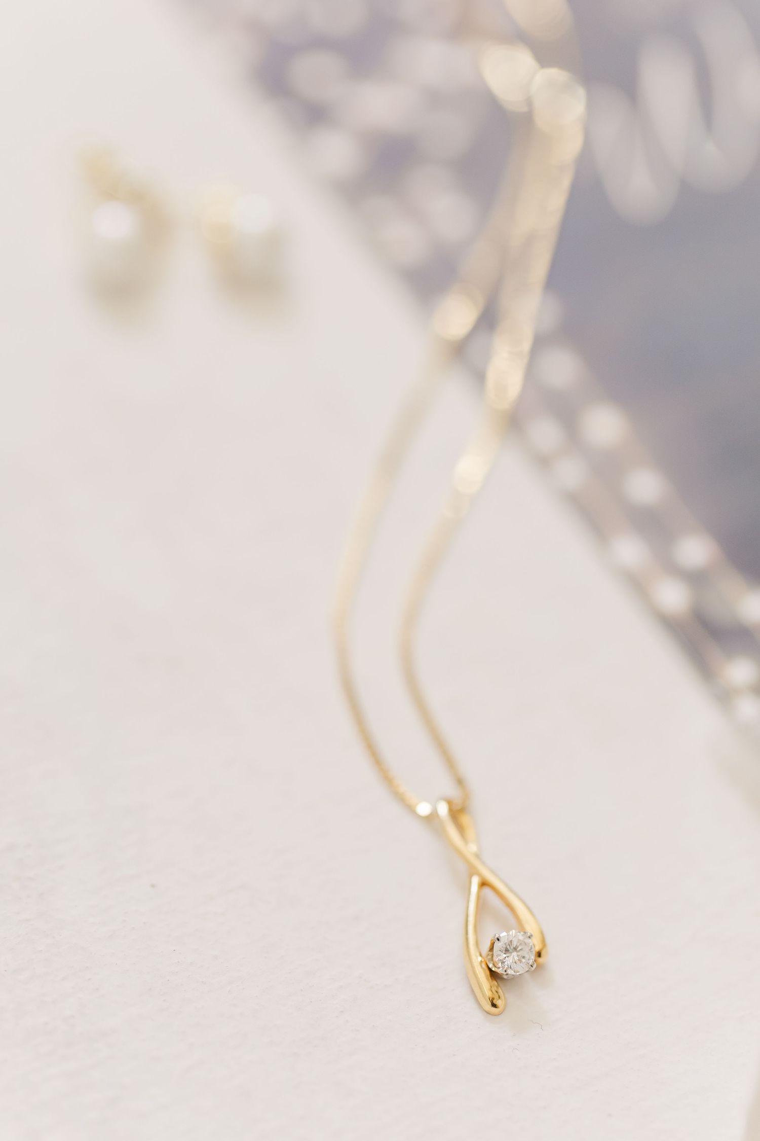 Delicate gold necklace with tiny diamond pendant sparkles against blurred light background.