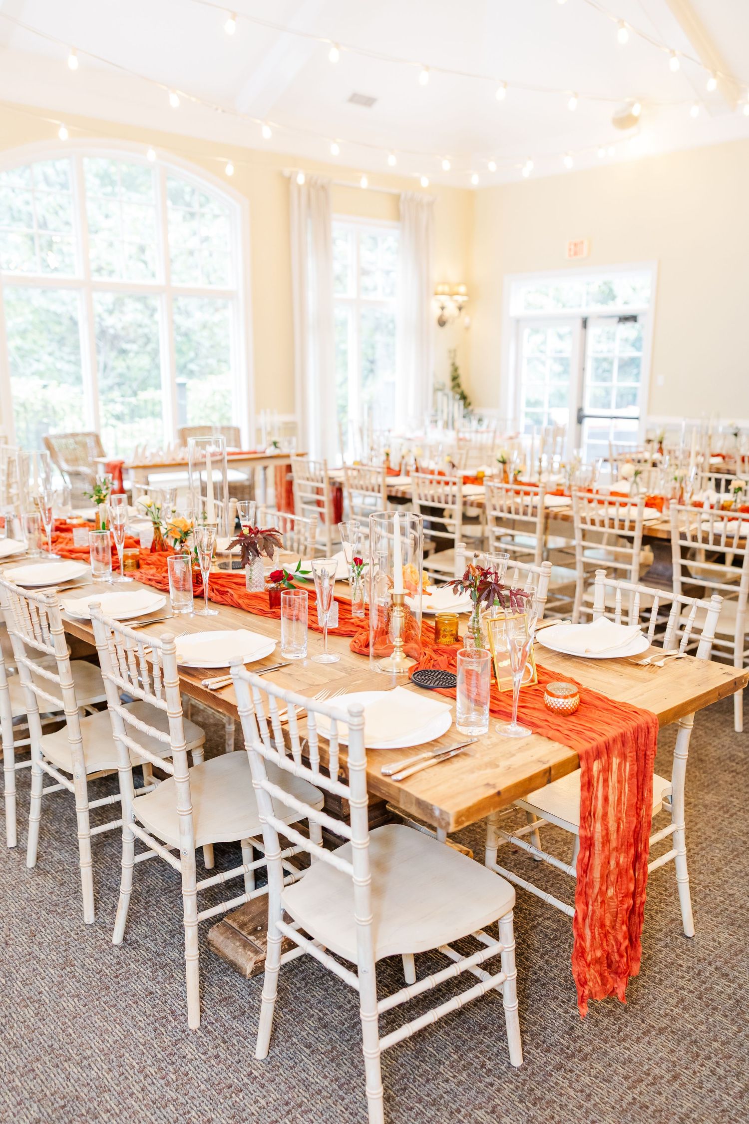Wedding reception venue with white chairs and orange table runners set up for dining.