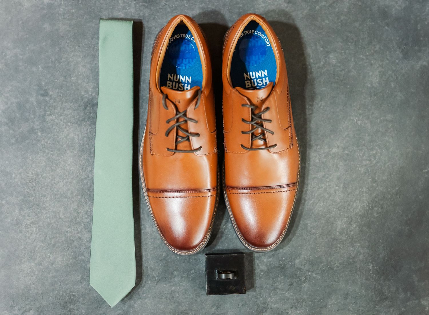 Brown leather dress shoes arranged in different angles on a gray textured surface.