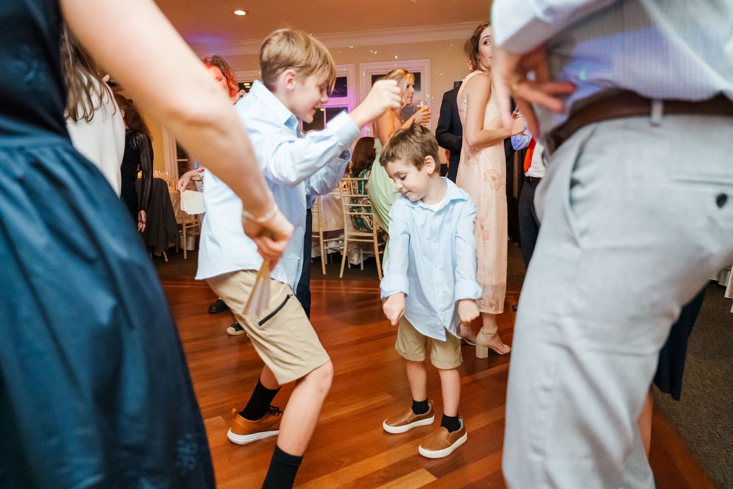 Wedding guests dancing at reception on wooden dance floor with casual attire.