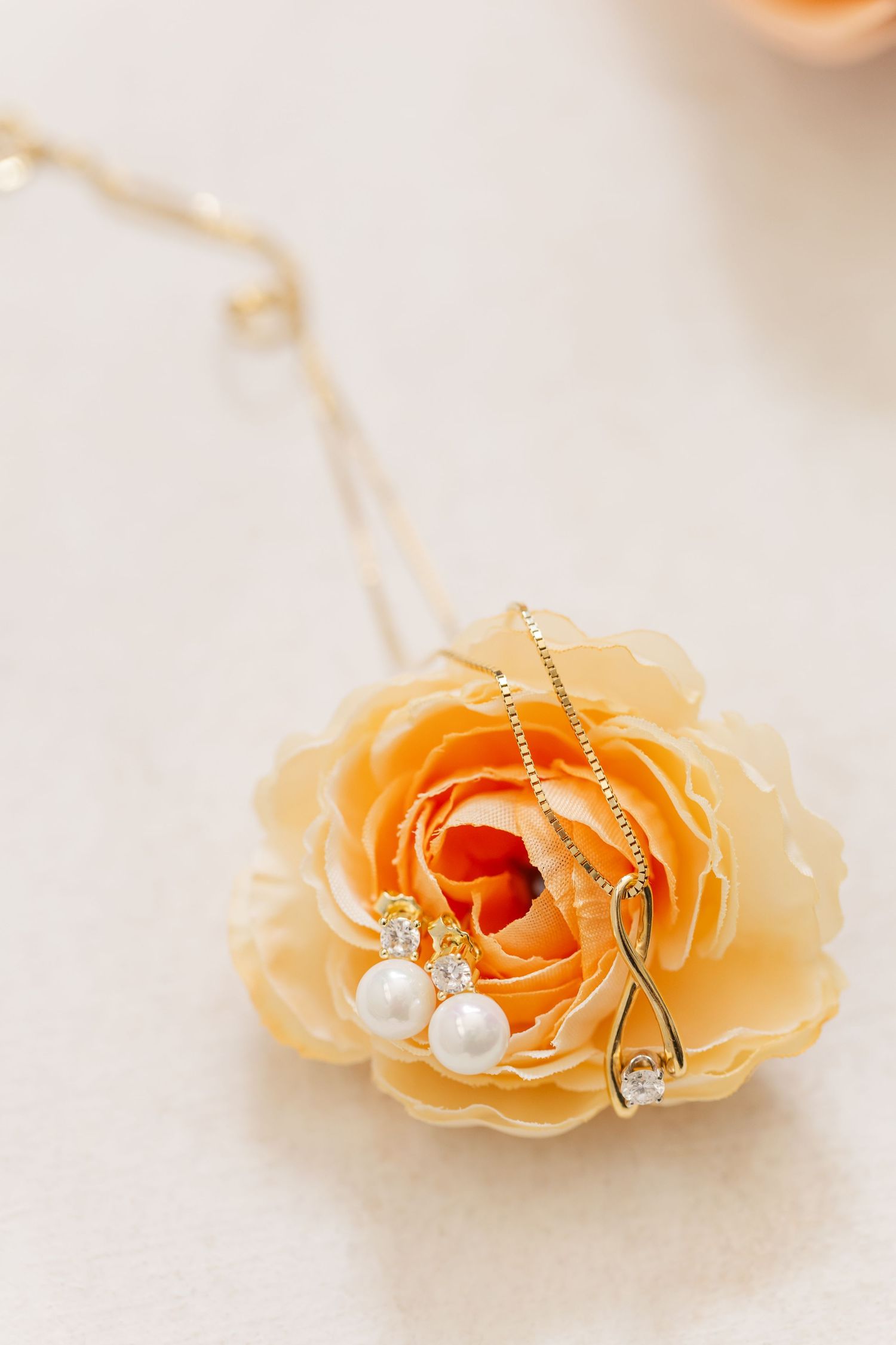 Delicate peach rose bloom with pearl and crystal jewelry necklace arranged on light fabric background.