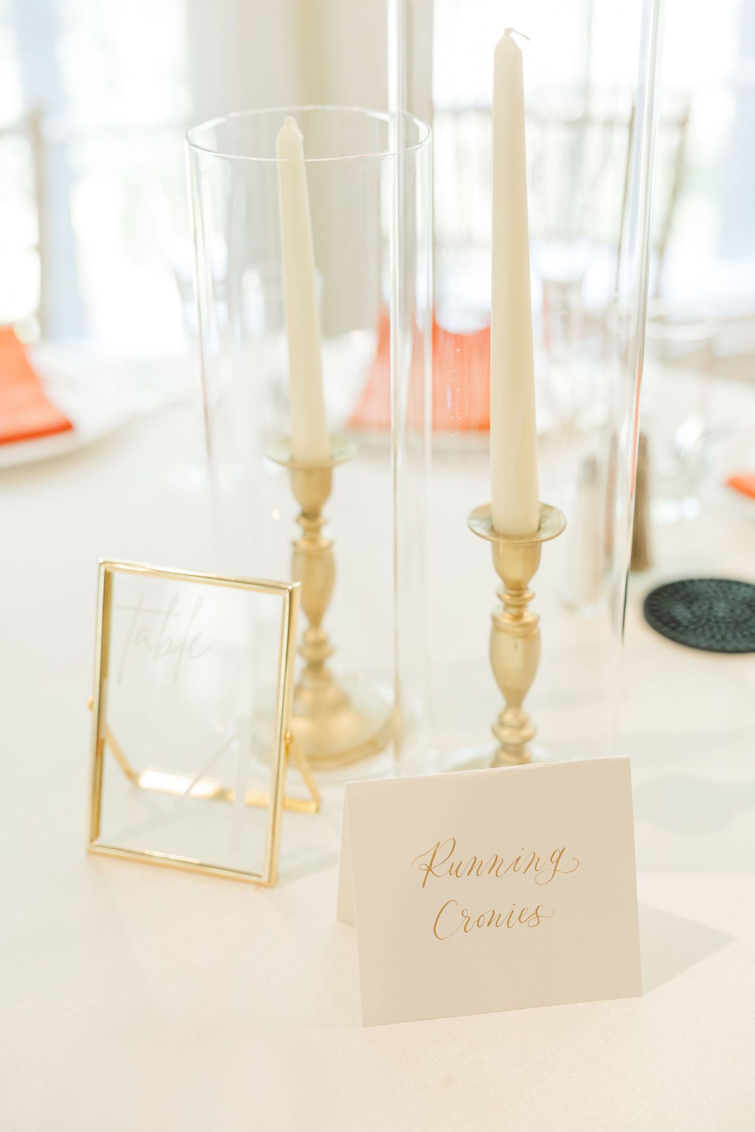 Wedding reception table settings with gold-framed place cards and white taper candles.