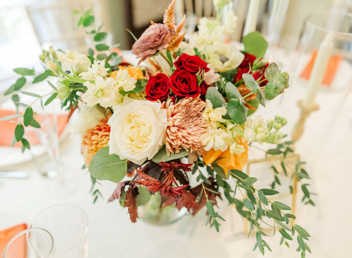 Elegant floral centerpiece with white roses, peach dahlias, red blooms and eucalyptus greenery arranged in a low vase.