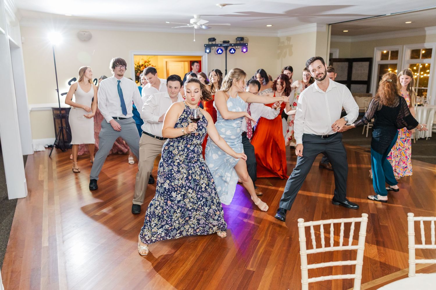 Wide angle view of wedding reception venue with guests dancing and white chairs.