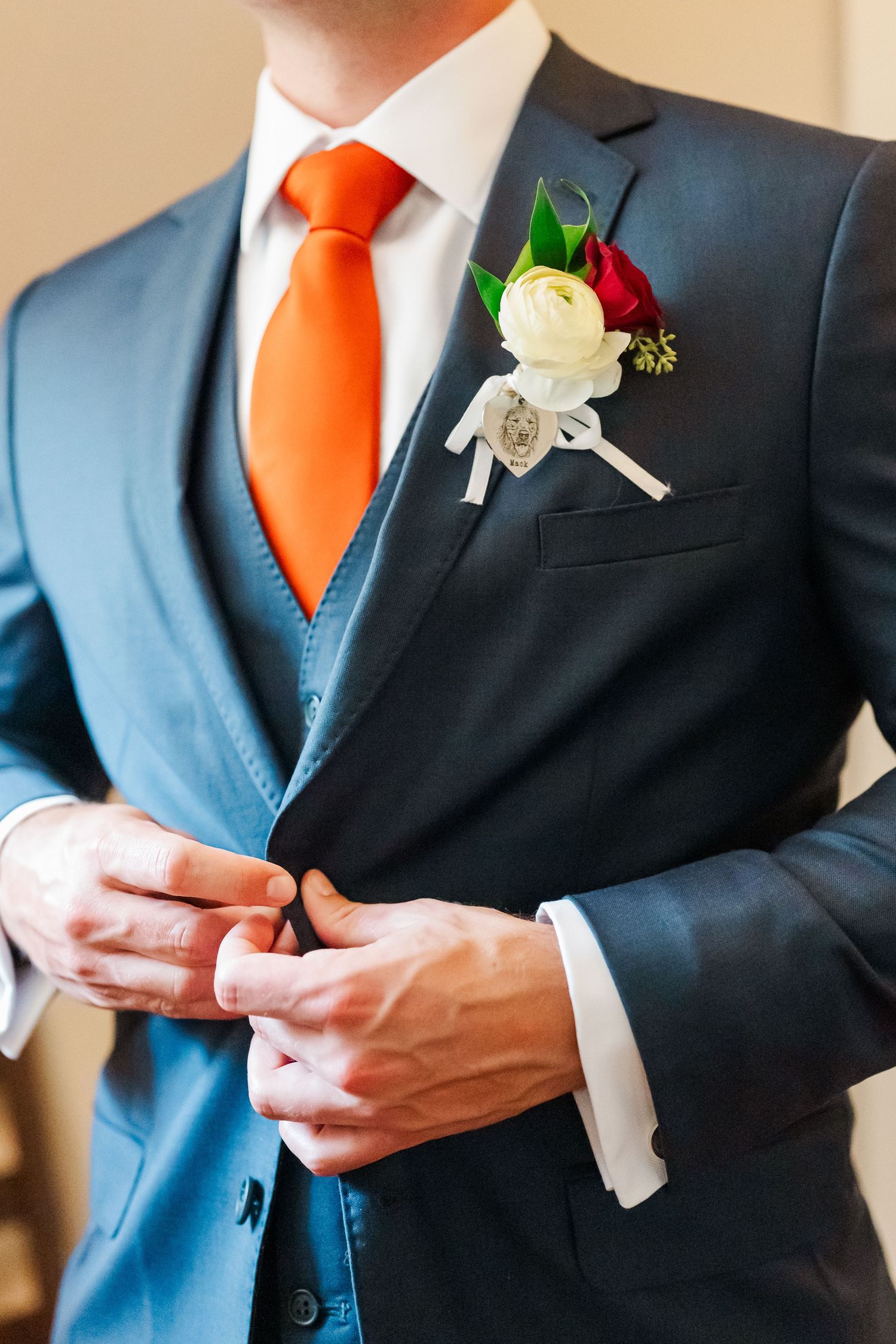 Groomsmen in black suits with bright orange ties and white boutonnieres stand together at a formal wedding.