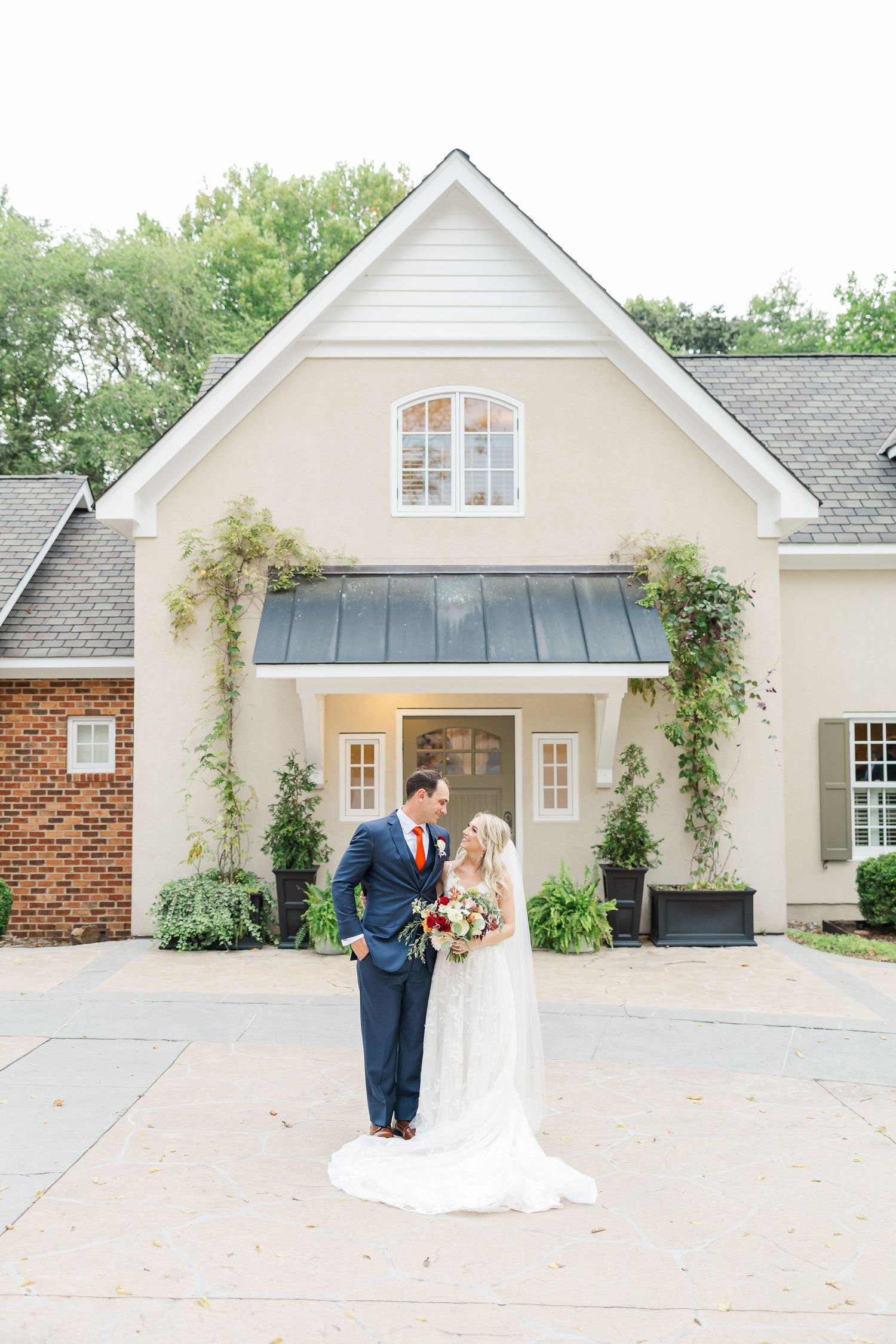 Couple dancing and twirling in front of a white church building with climbing vines and brick accents.