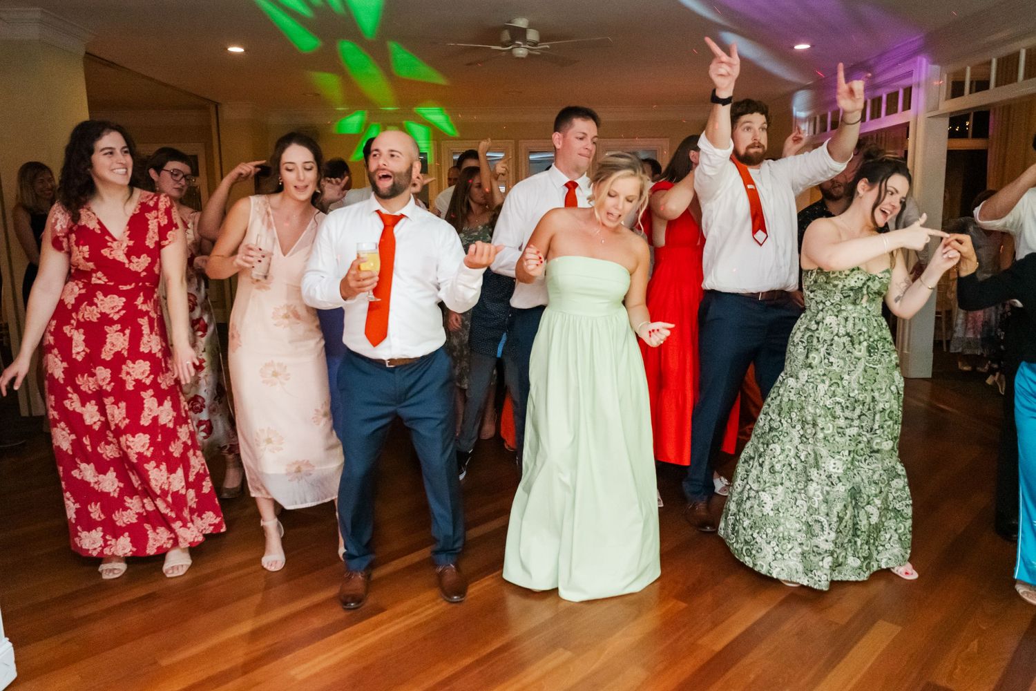 Wedding guests dancing and celebrating on a dance floor illuminated with colorful lights.