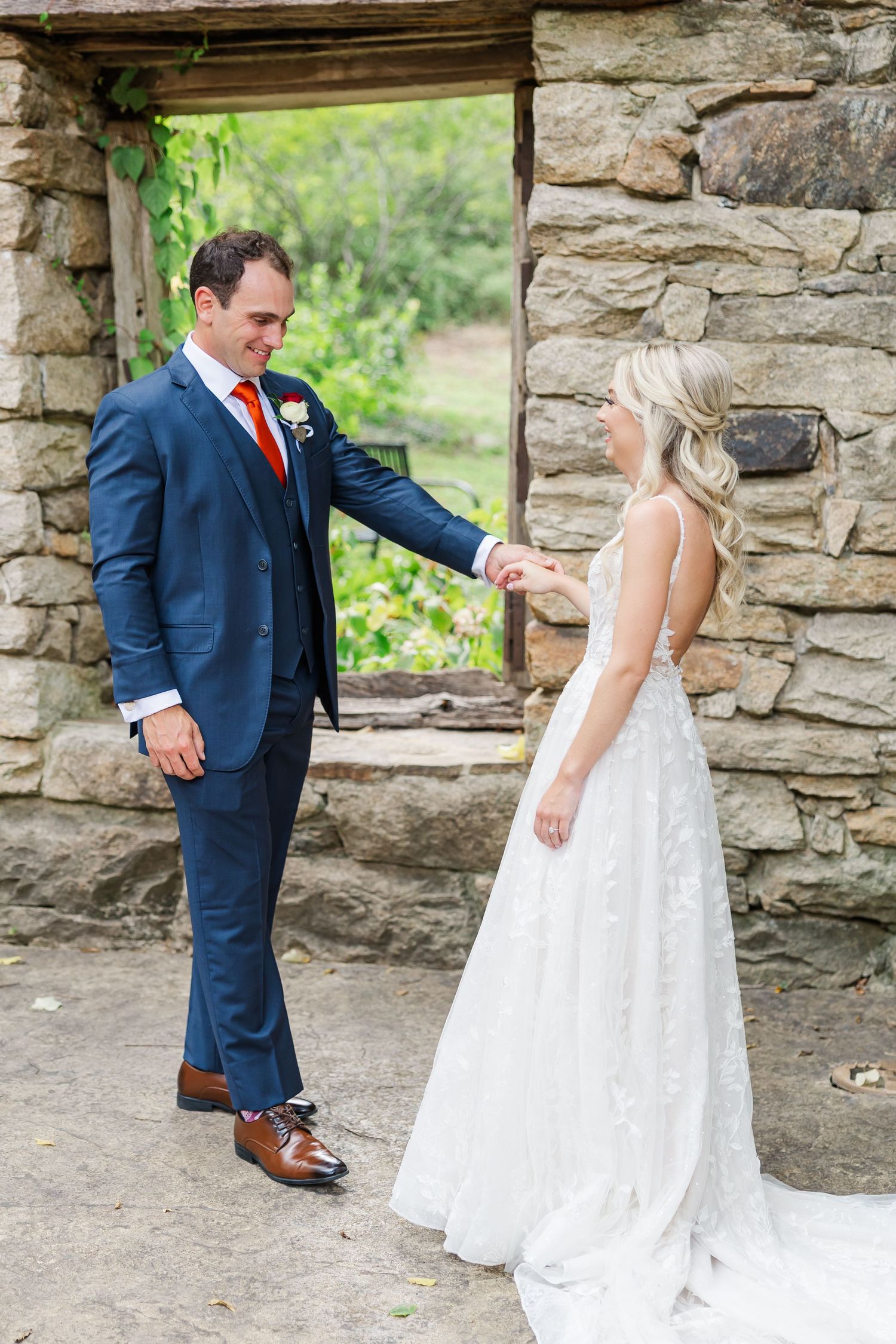 Bride and groom share a playful dance moment against a rustic stone wall backdrop.