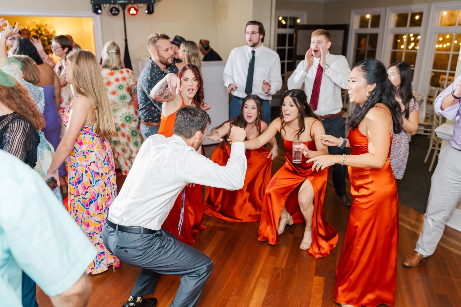Wedding party dances energetically with bridesmaids in red dresses on the dance floor.