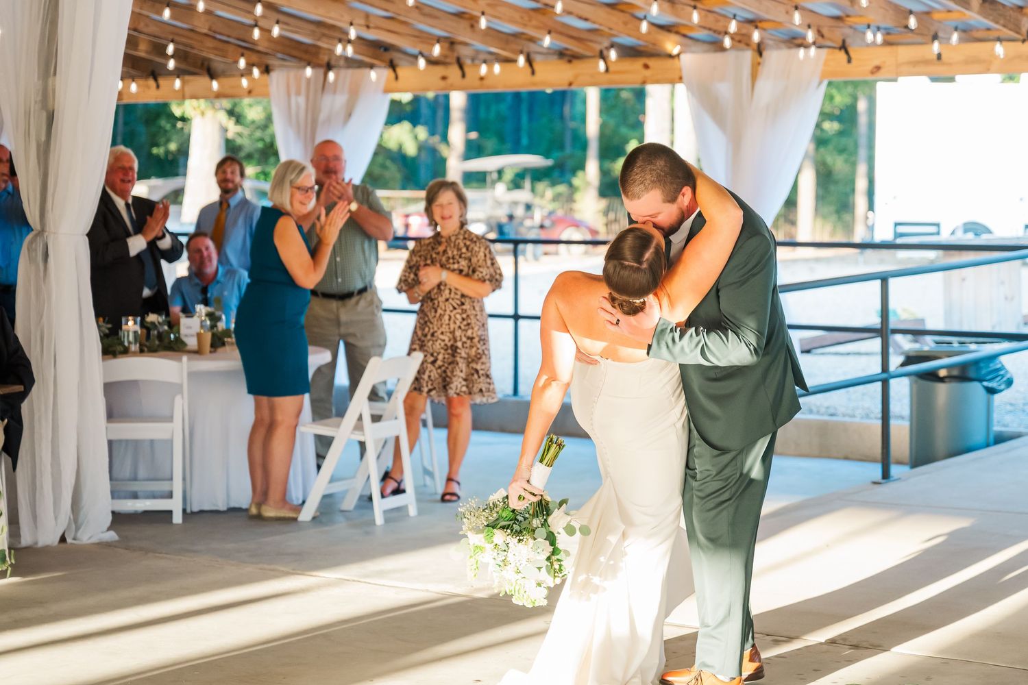 Bride and groom share their first dance embrace at an outdoor wedding reception with string lights.