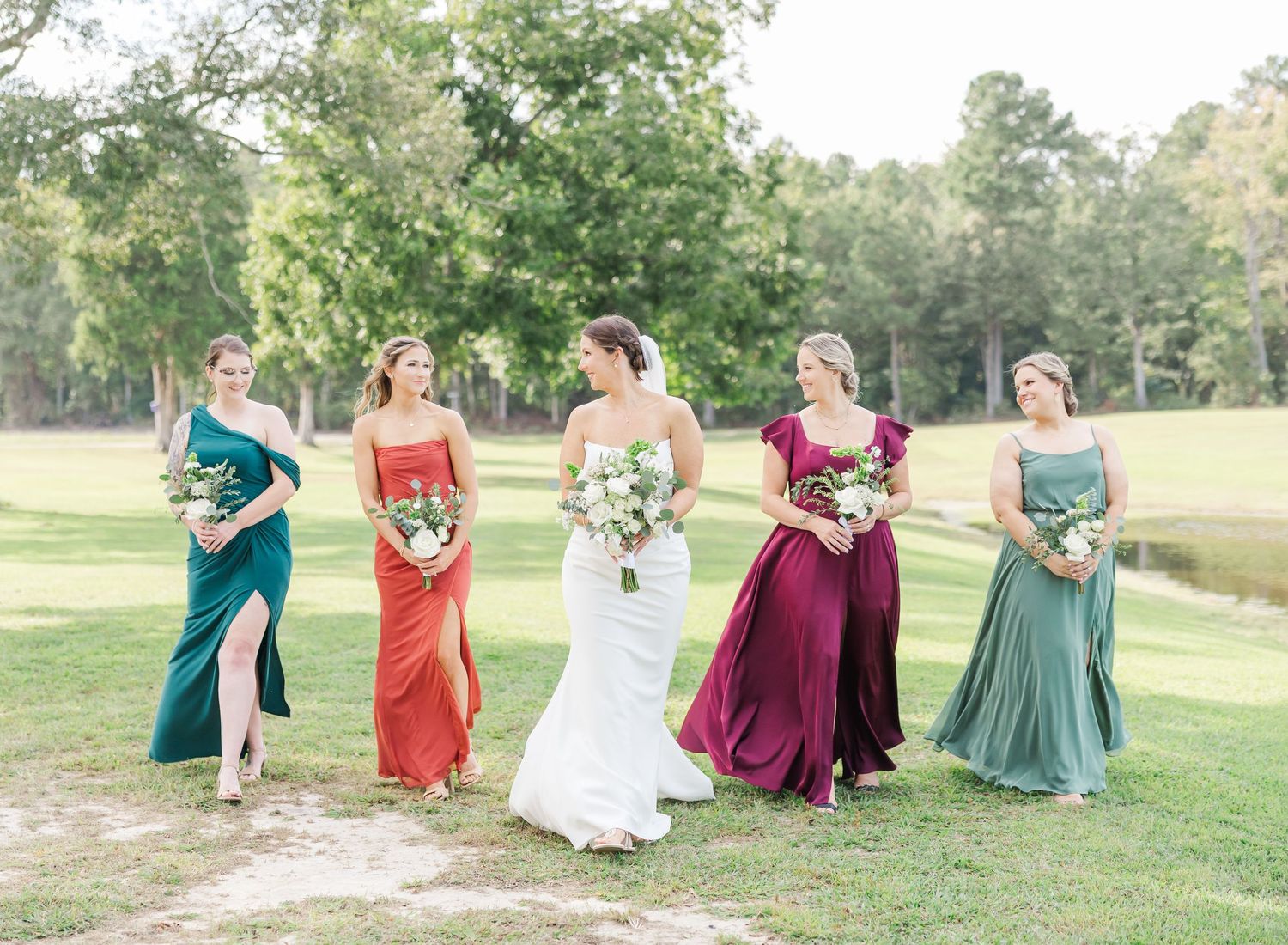 Wedding party in colorful dresses walking and laughing together on a grassy lawn.