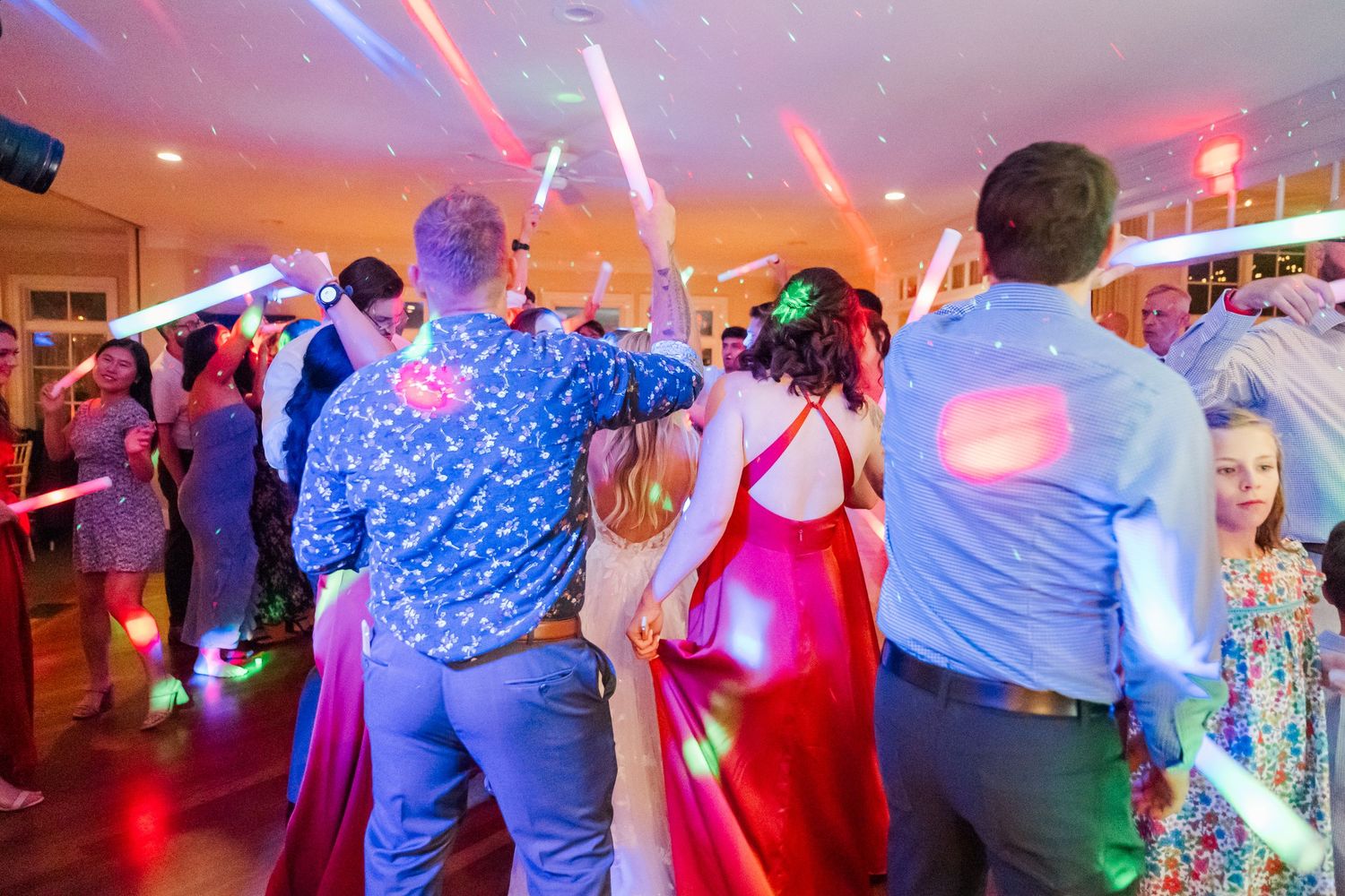 Dance floor filled with party guests under colorful blue and pink lighting effects.