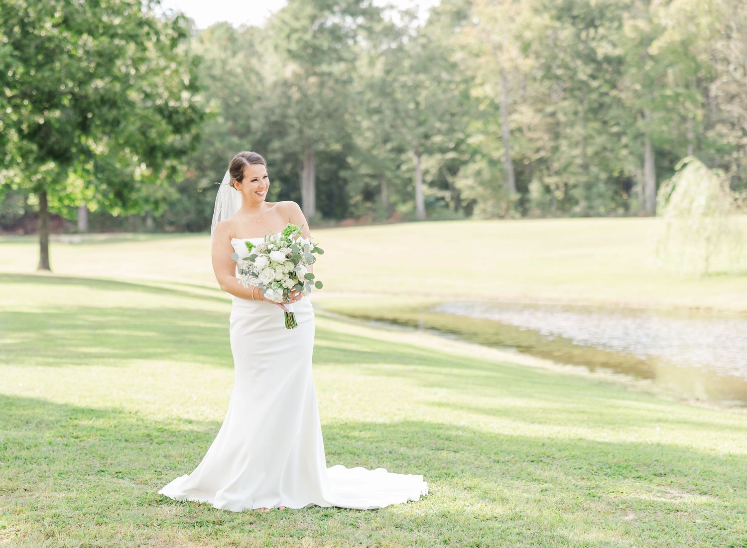 A bride in a flowing white wedding dress poses gracefully in a sunlit meadow during golden hour.