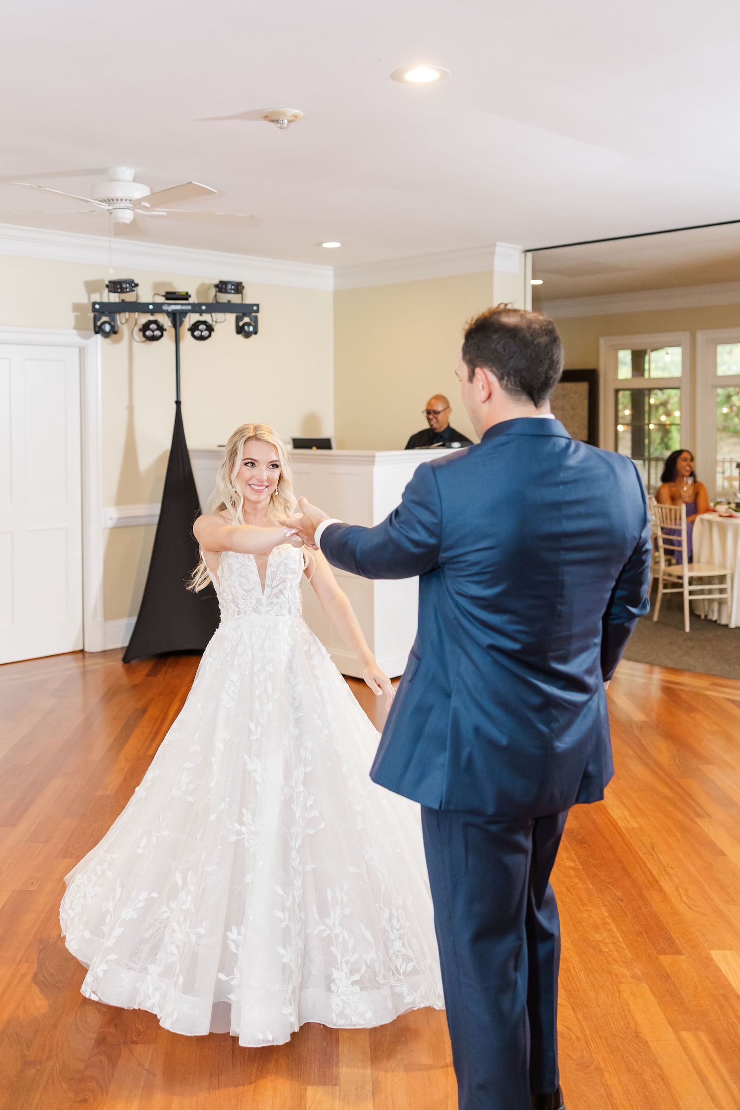 Couple dancing in an elegant reception venue with hardwood floors and natural lighting.