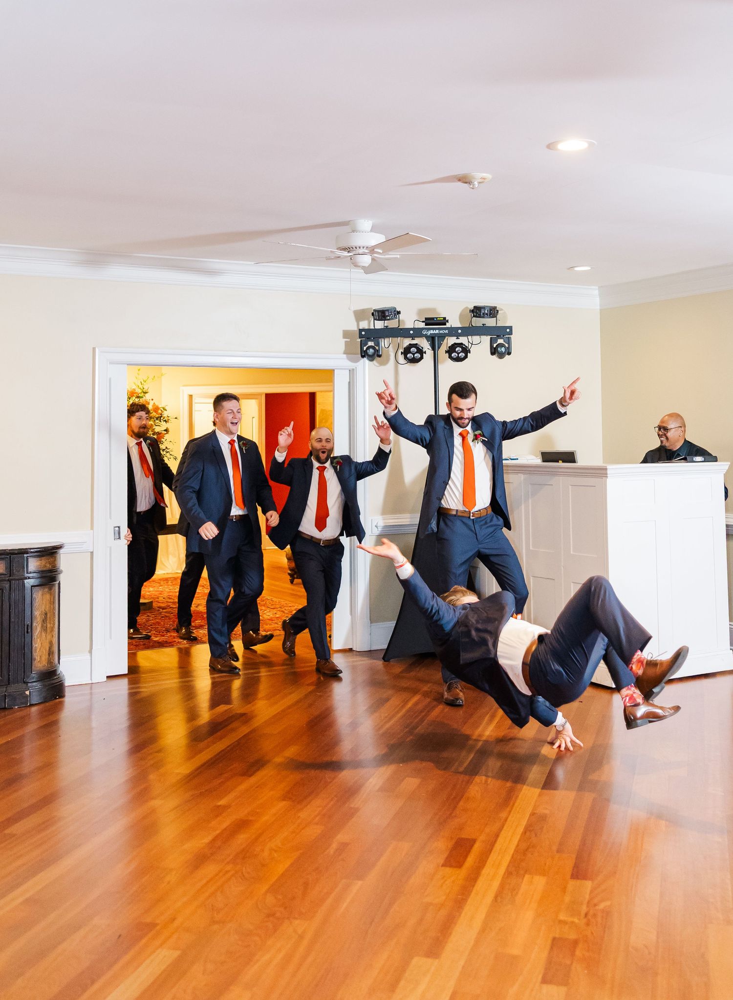 Groomsmen perform synchronized jumping poses on a hardwood floor during wedding photo session.