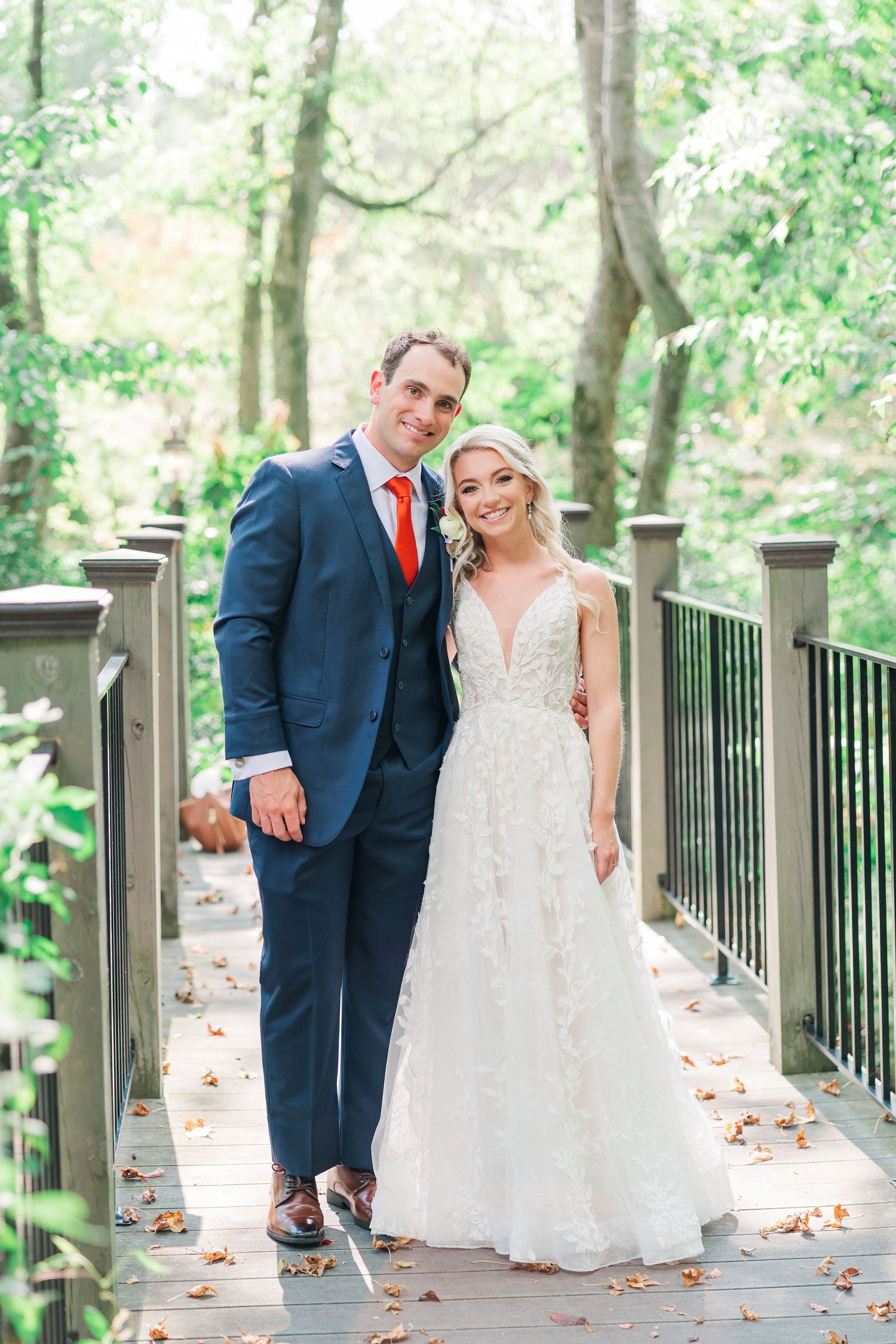 Couple shares a playful moment on a wooden bridge walkway surrounded by lush greenery on their wedding day.