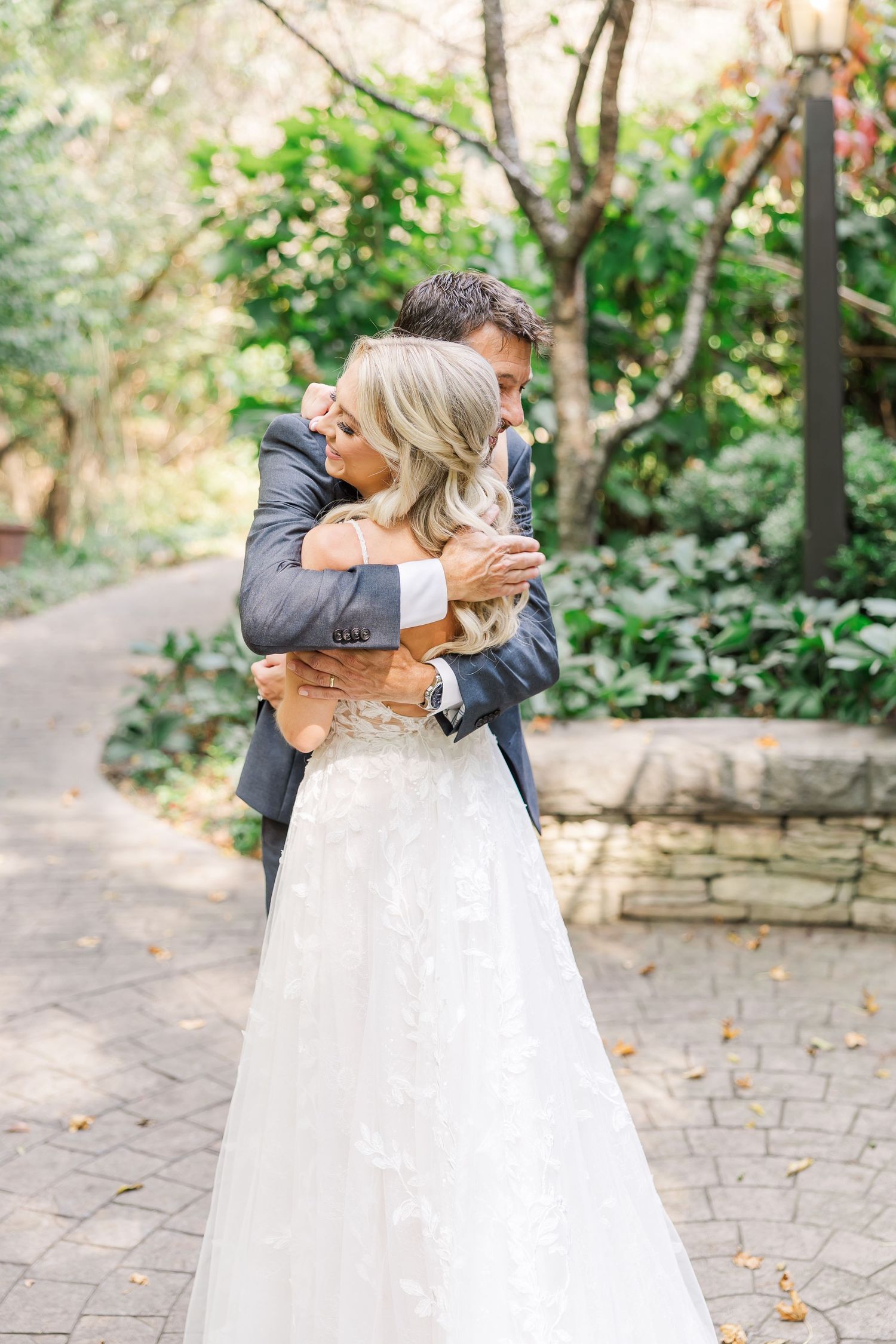 Couple shares romantic embrace on a stone paved garden path surrounded by lush greenery.