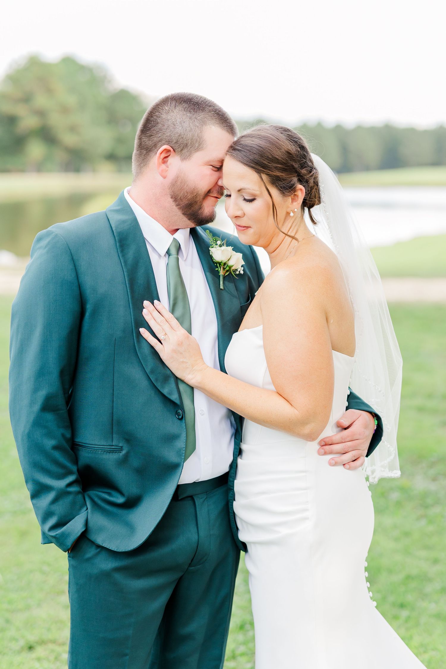 A couple shares intimate moments in a series of romantic outdoor wedding photos wearing green suit and white dress.