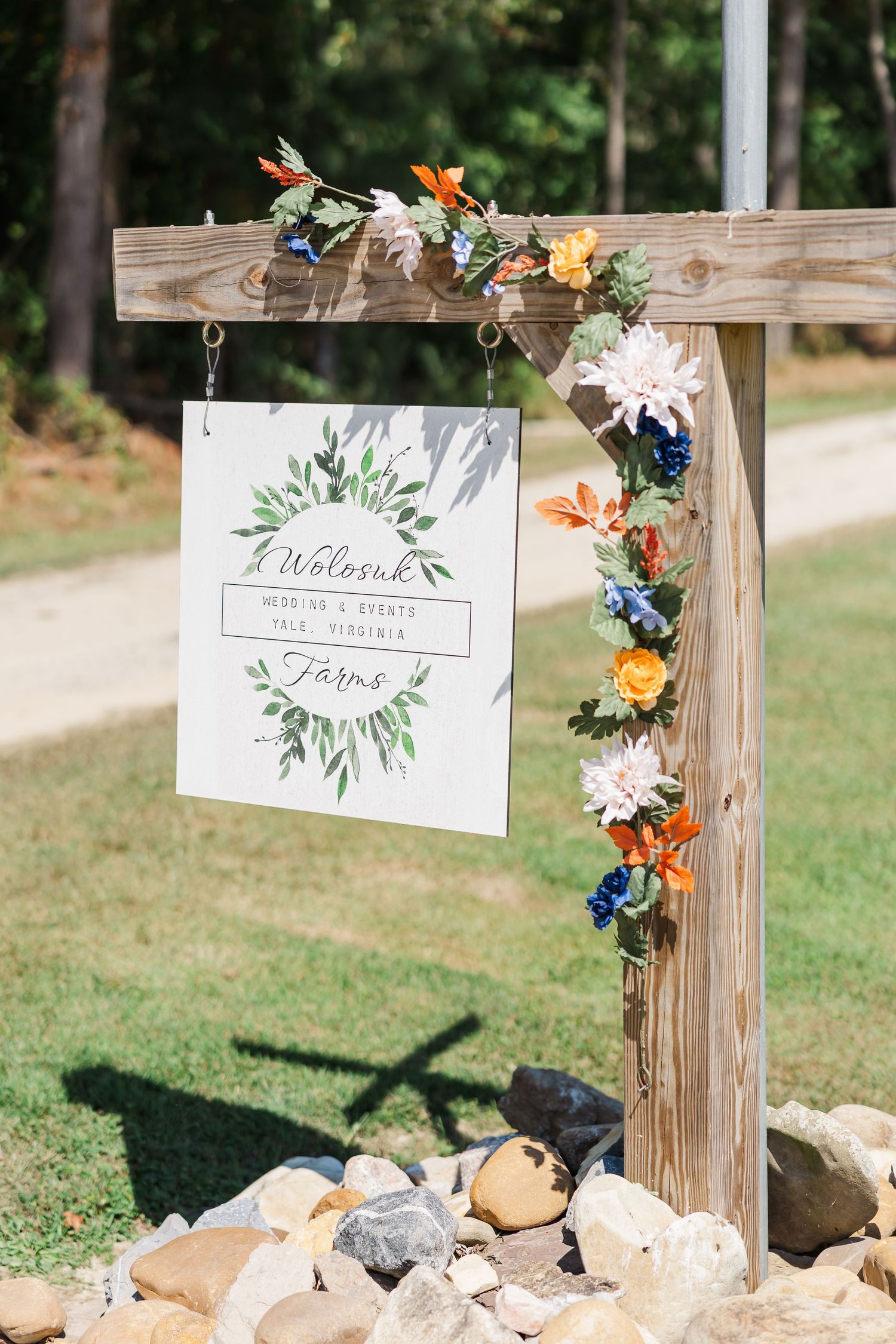 Rustic wooden posts display elegant wedding signage with floral decorations against a green lawn backdrop.