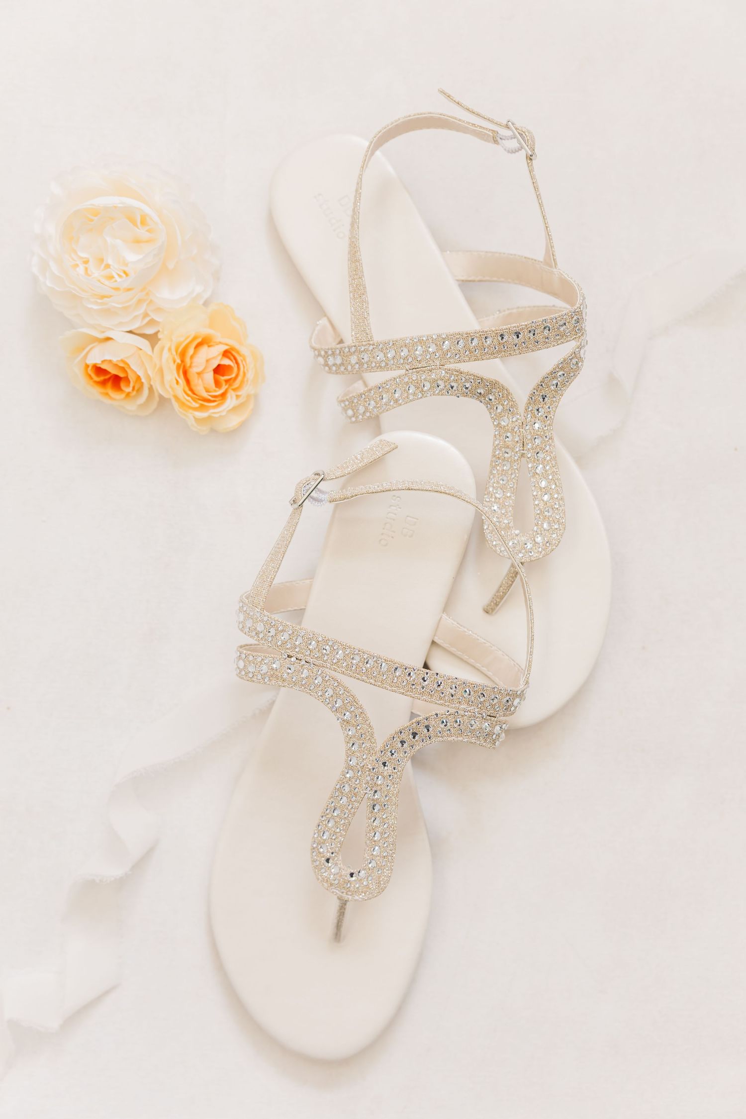 Elegant white sandals with crystal embellishments and delicate flowers arranged on a light background.