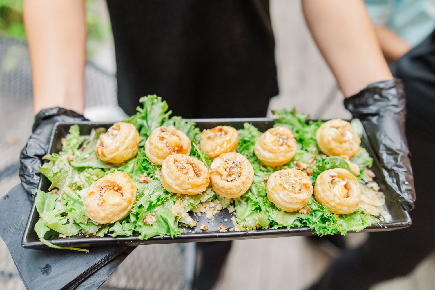 Catering staff serve elegant appetizer plates with shrimp and fresh greens on black rectangular platters.