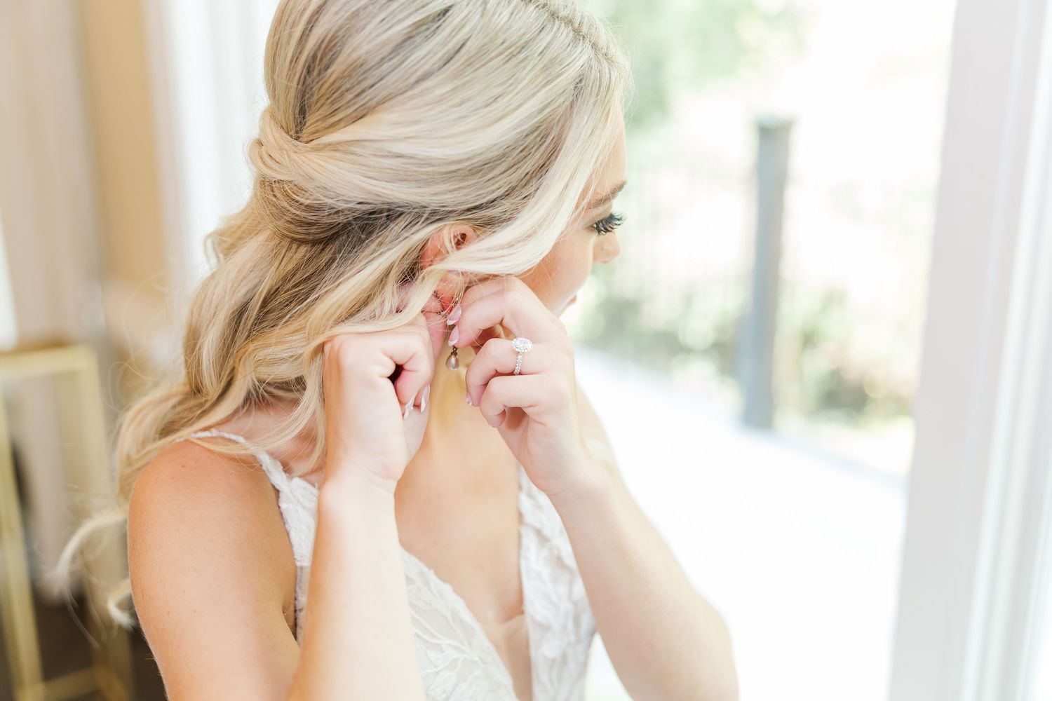 A bride getting ready for her wedding day, sitting by a window in a white robe while having her makeup done.