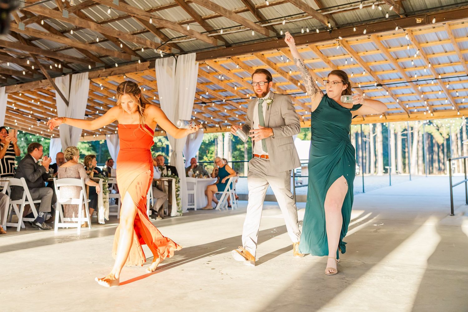 Three guests in colorful formal attire perform a choreographed dance at an elegant outdoor wedding reception.