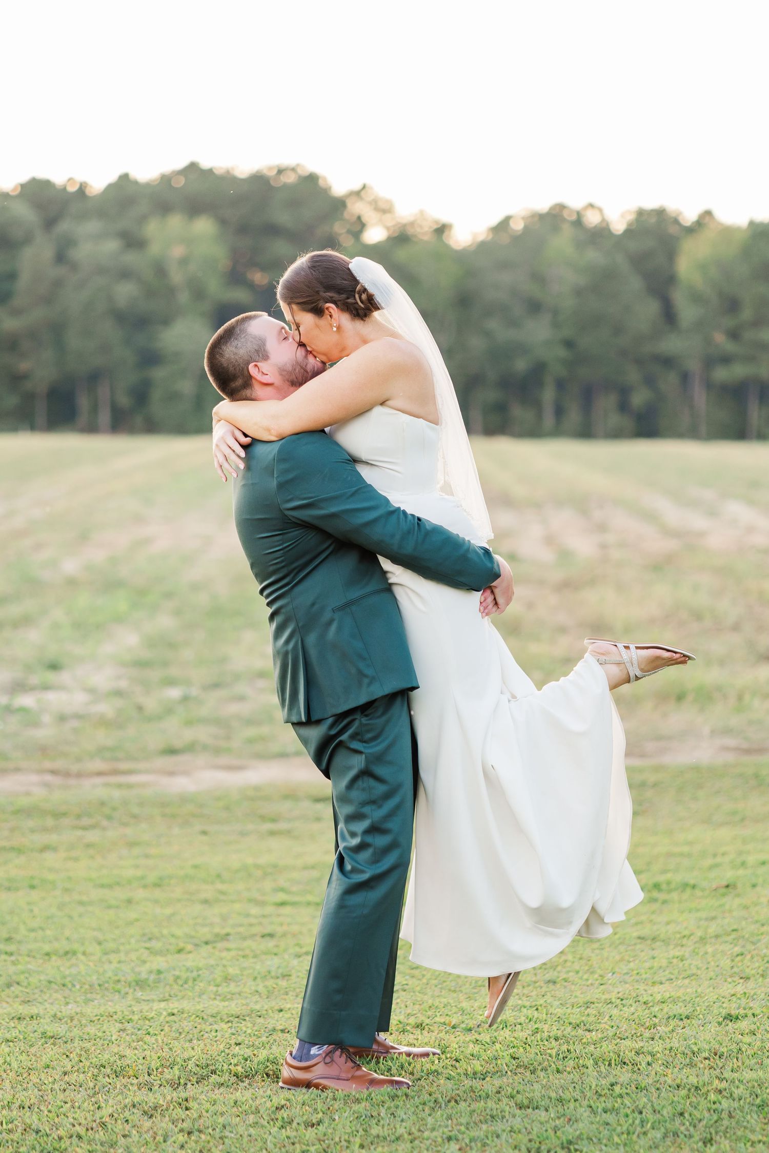 A joyful wedding couple embraces in a playful lift pose against a scenic outdoor backdrop.