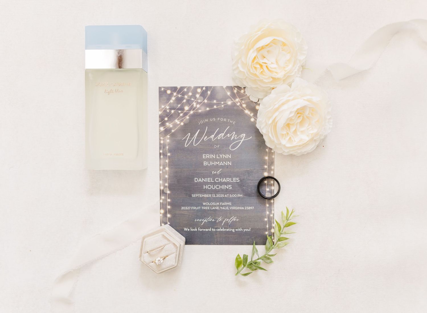 Wedding invitation suite with cream roses, gray stationery, and delicate greenery arranged on light marble surface.