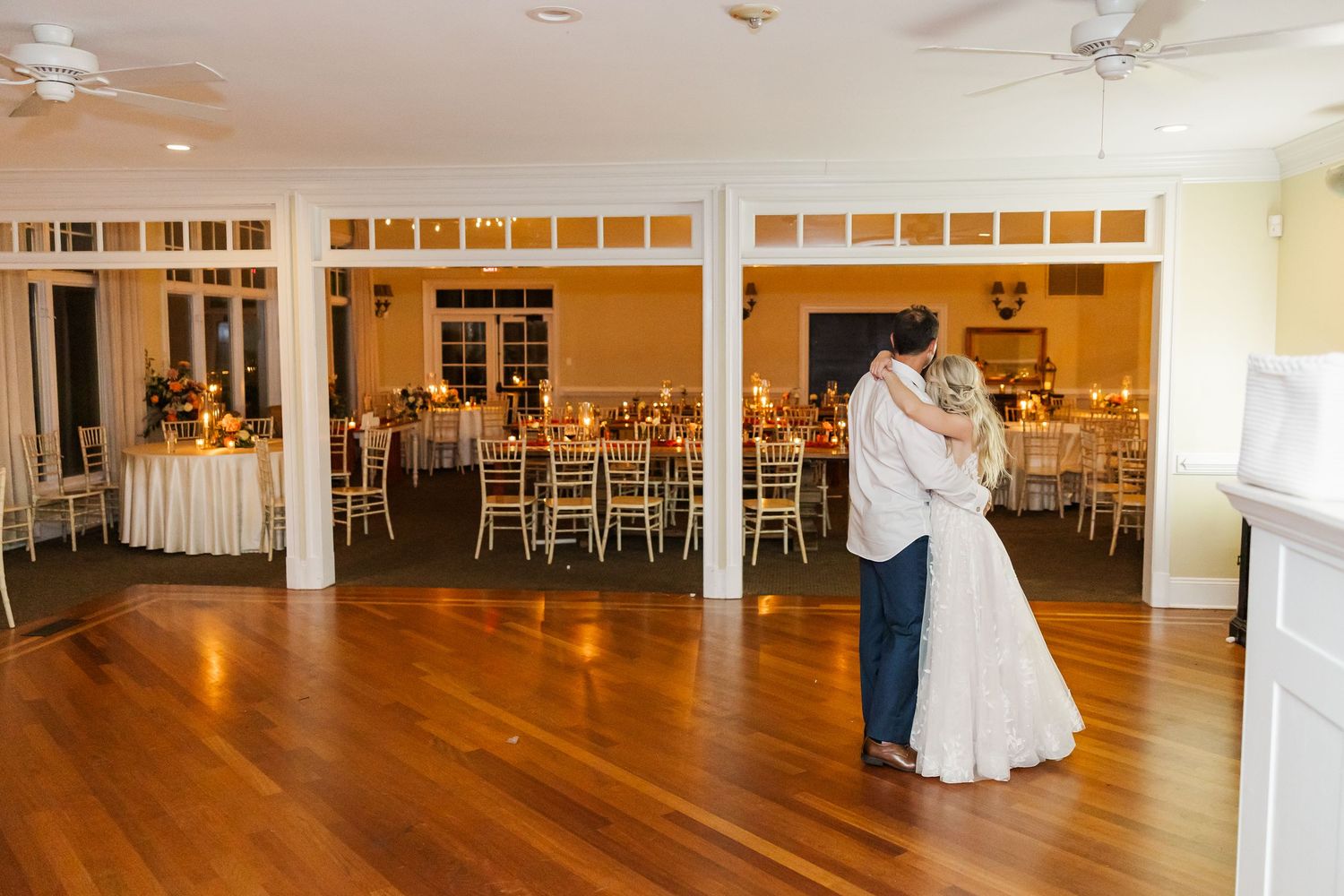 Panoramic view of an elegant reception hall with hardwood floors and white chairs.