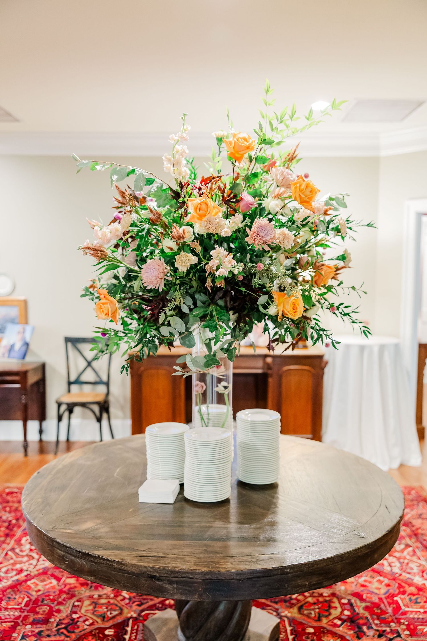 Elegant floral centerpiece with peach and orange blooms on a round wooden table.