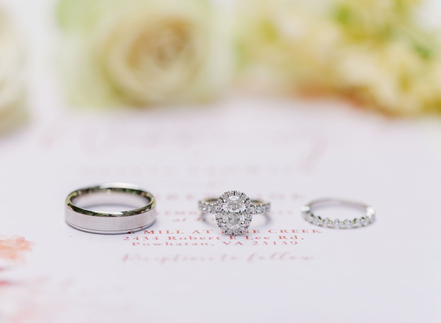 Three elegant wedding rings displayed on soft pink paper, including a diamond engagement ring and matching bands.