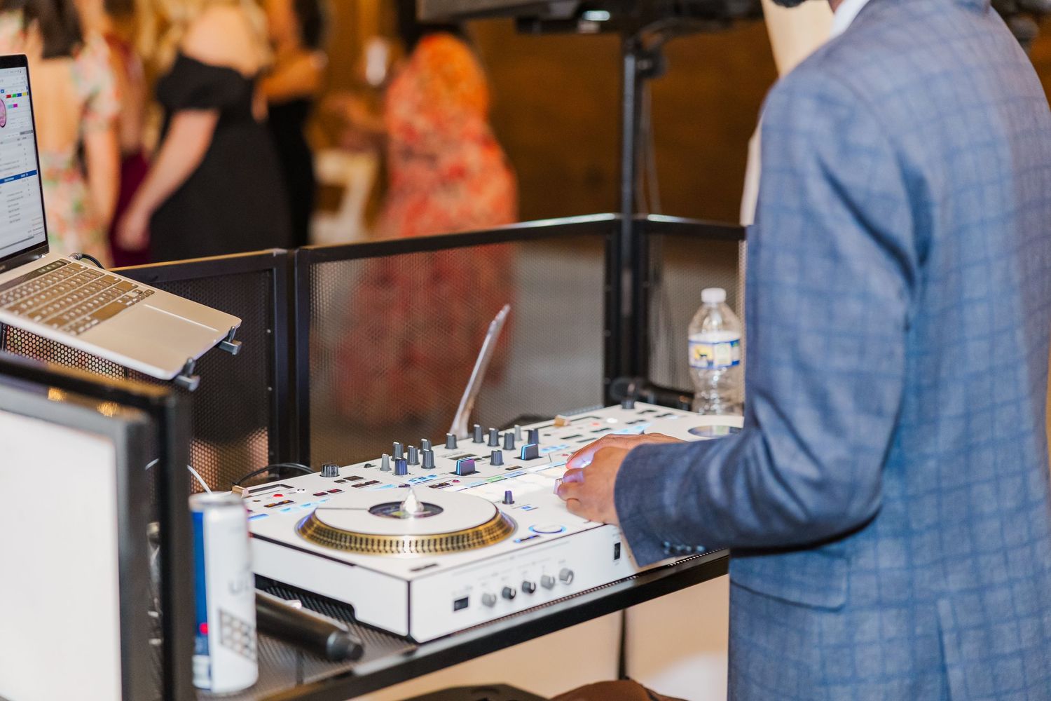 A DJ in a blue suit operates professional turntables and mixer equipment at a wedding reception.