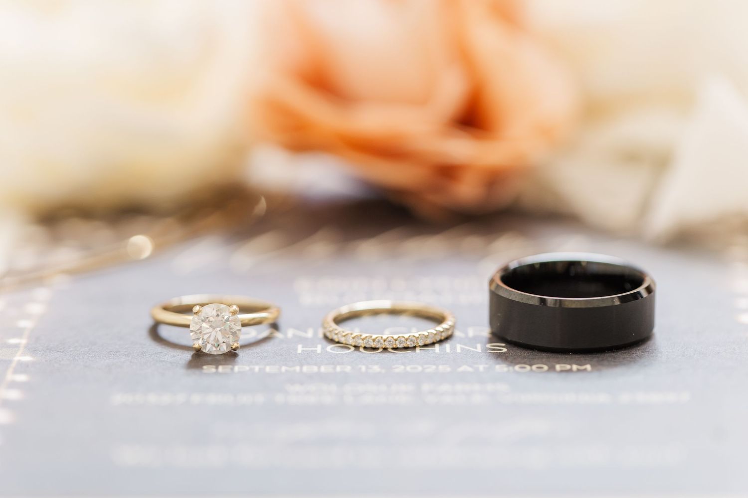 Wedding rings displayed on a light gray surface with soft pink roses in the background creating a romantic setting.