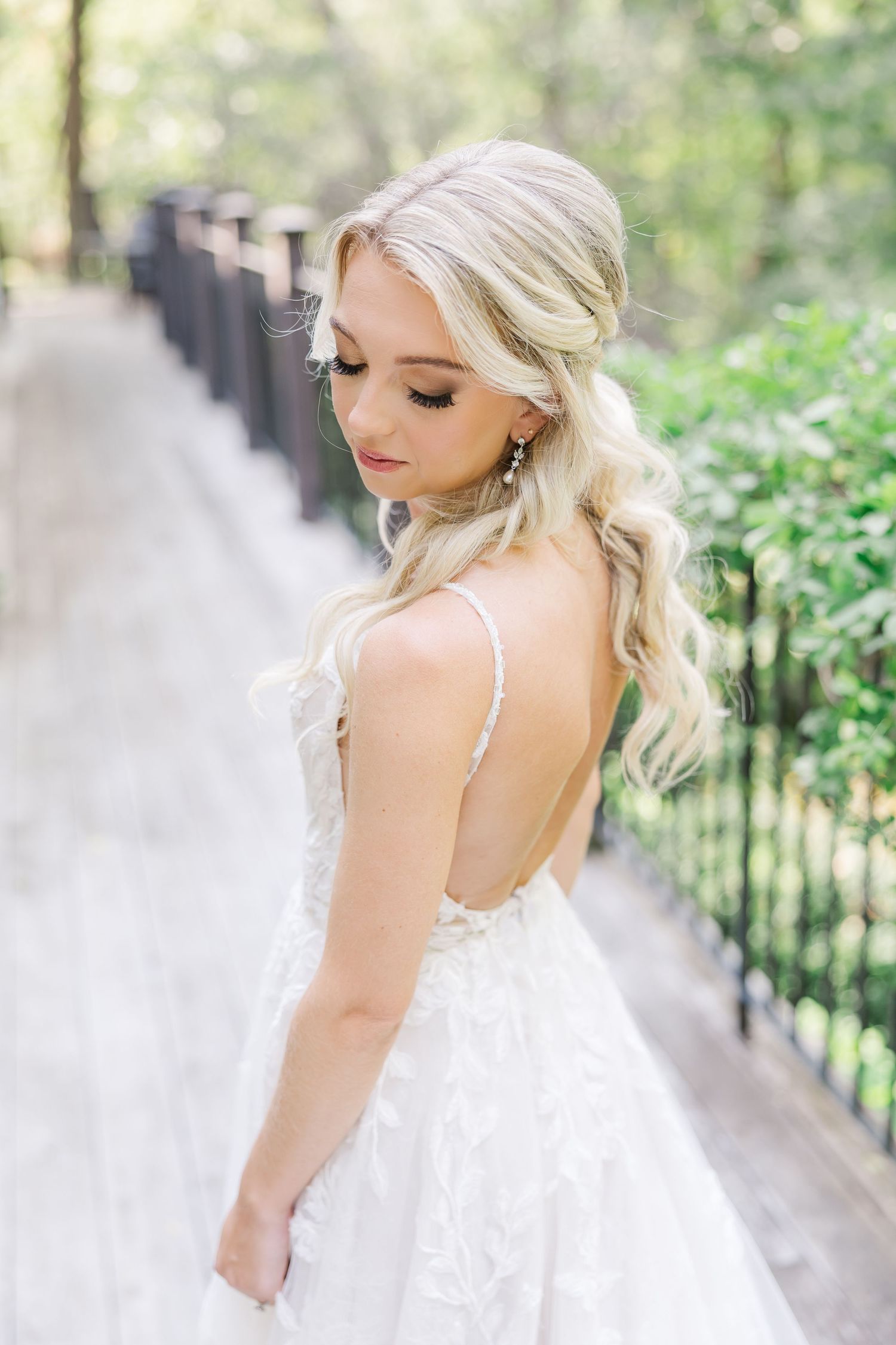 A bride in a flowing white lace gown poses elegantly in a garden setting with soft natural lighting.
