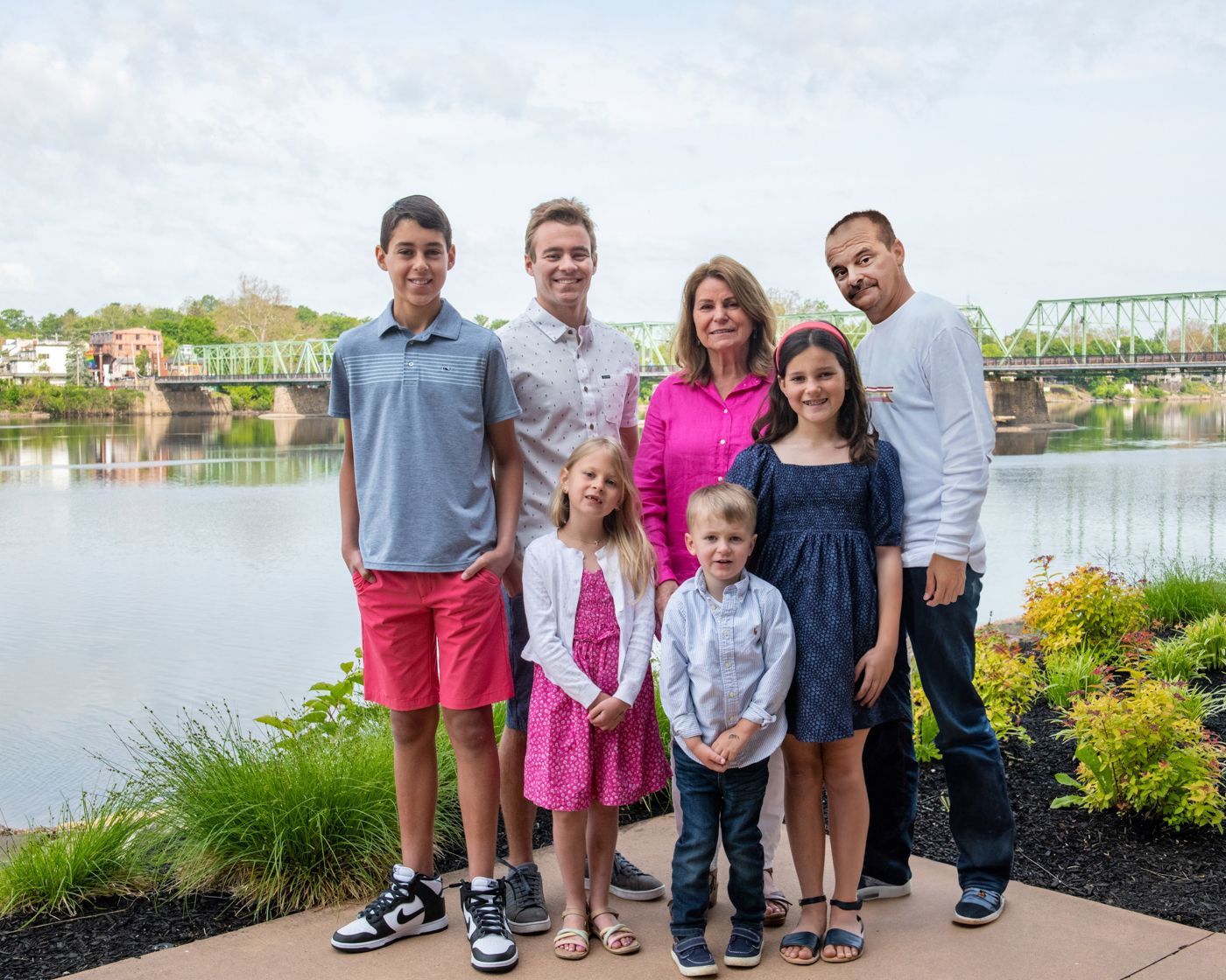 Family portrait by a riverside with a green bridge visible in the distance.