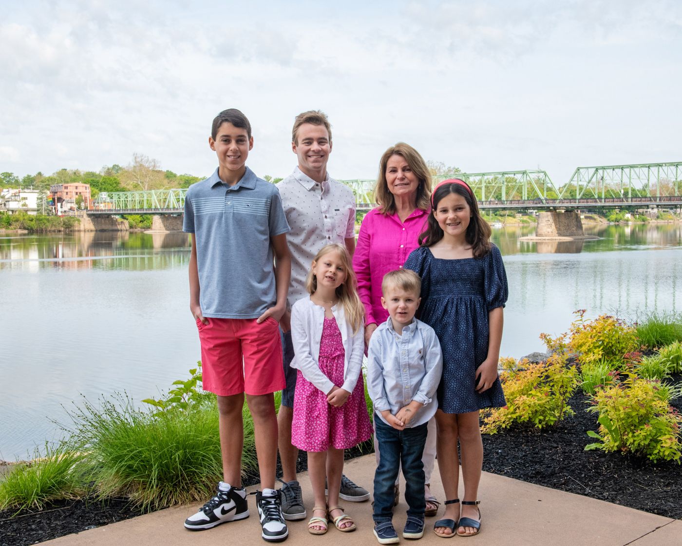 Group photo of several people standing together by a river with a bridge in the background.