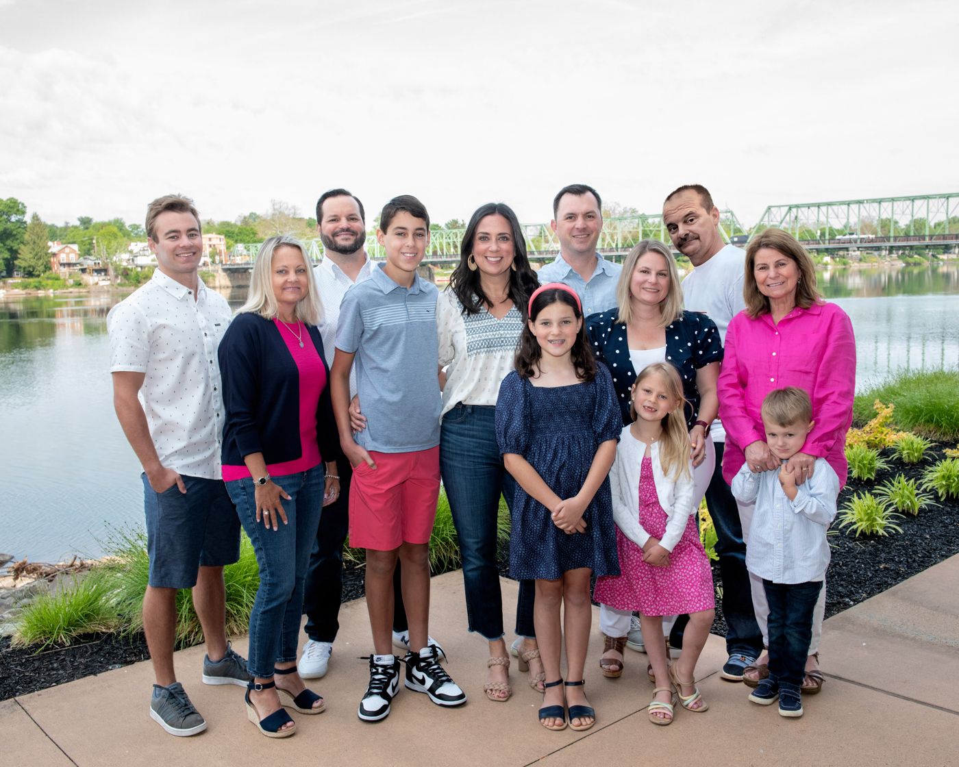 Group photo of people wearing mix of bright and casual clothes posed near water with bridge backdrop.