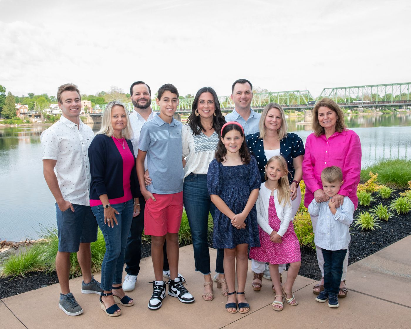 Large group portrait of people in casual attire standing by a waterfront with bridge view.