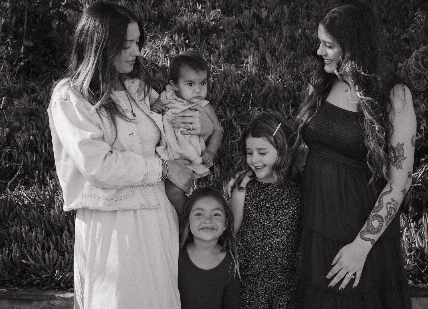A black and white candid photo shows two adults with children sharing a joyful moment together outdoors.