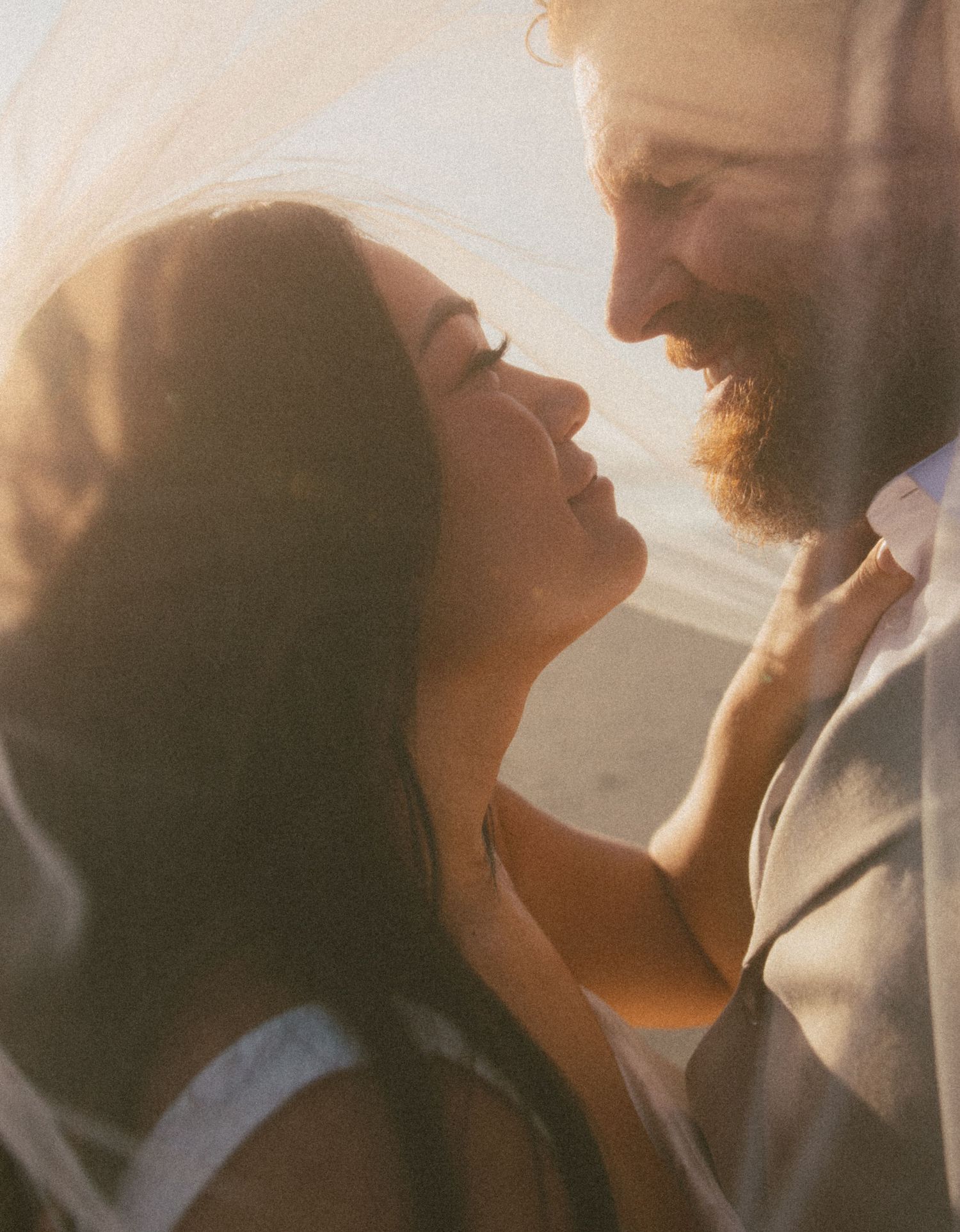 A couple shares an intimate moment in warm sunlight, with one person's beard and the other's dark hair silhouetted.