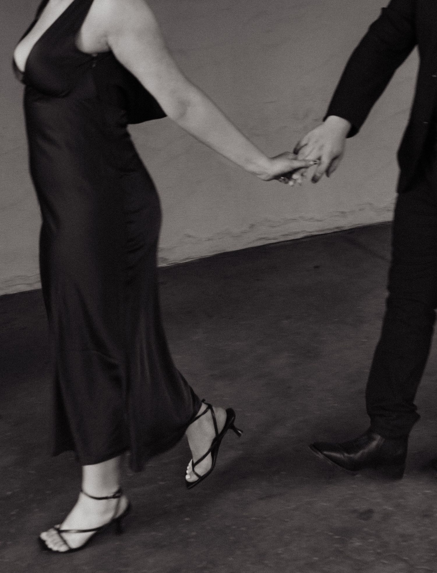 San diego Couples sessionBlack and white photo showing two people holding hands while dancing, focusing on their formal attire and footwear.