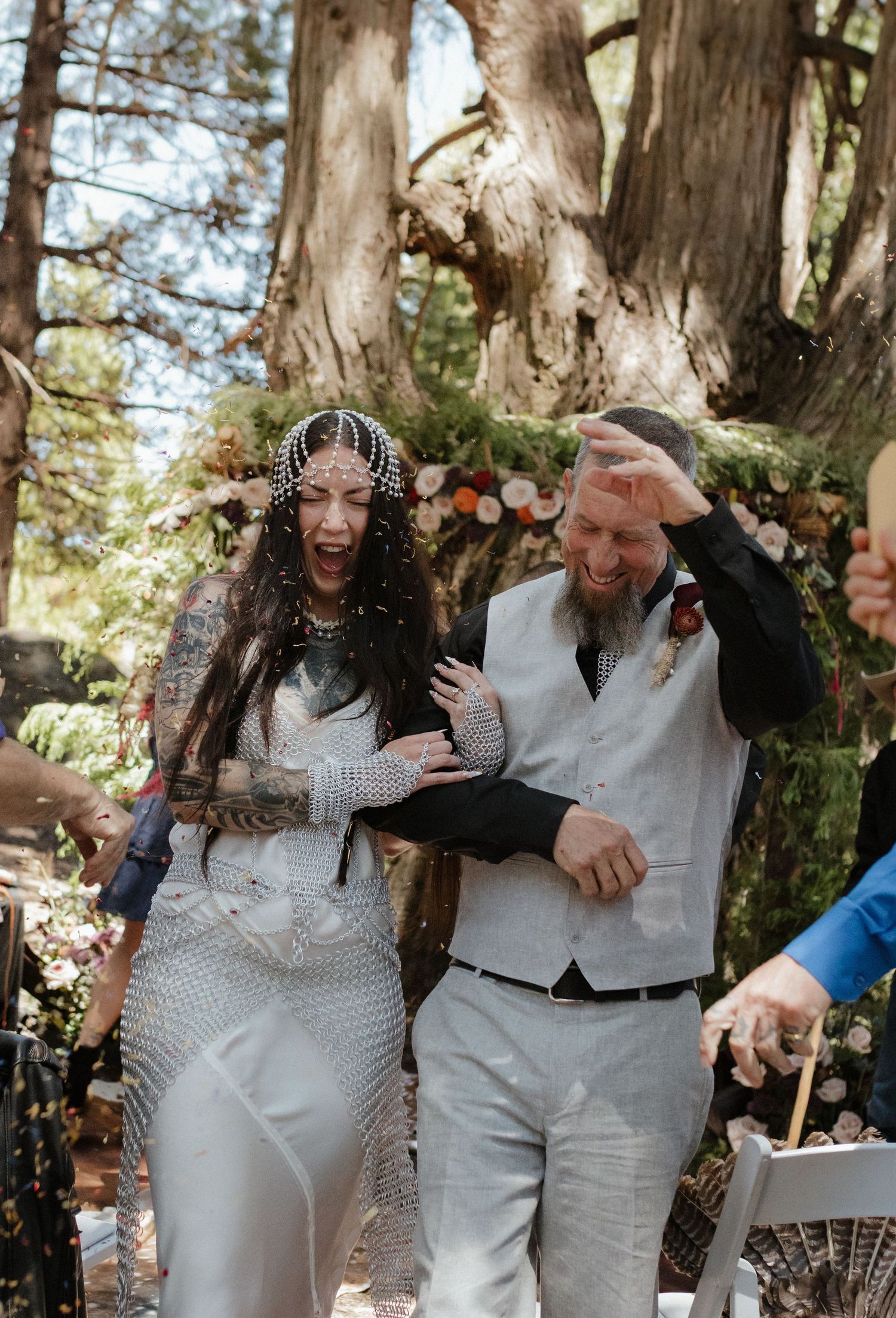 Happy couple shares candid laughter during outdoor wedding celebration in wooded setting.