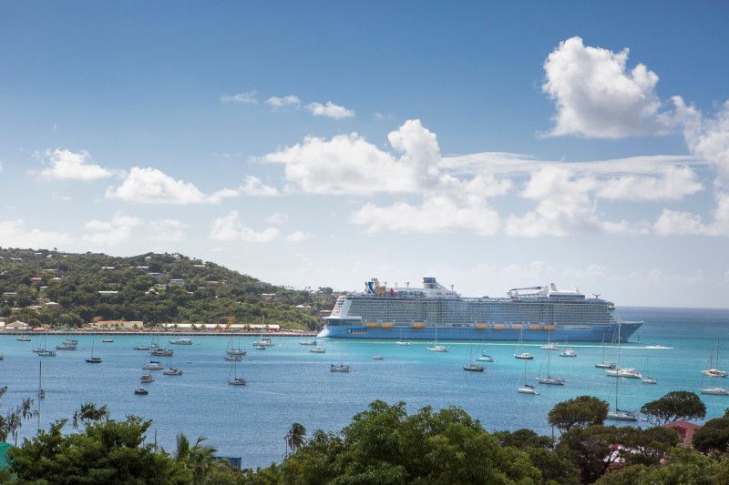Multiple cruise ships and boats dot the turquoise Caribbean waters near a tropical island harbor on a sunny day.