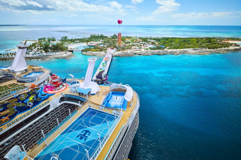 Aerial view of cruise ships docked at tropical island ports with vibrant turquoise waters and sports facilities onboard.