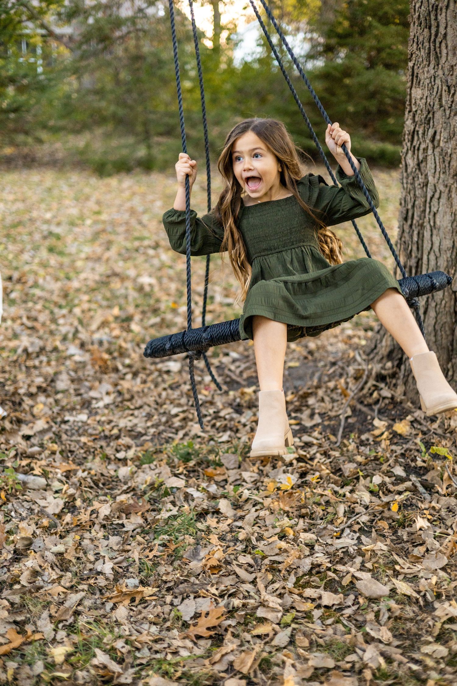 Person in green dress swinging joyfully among fallen autumn leaves.