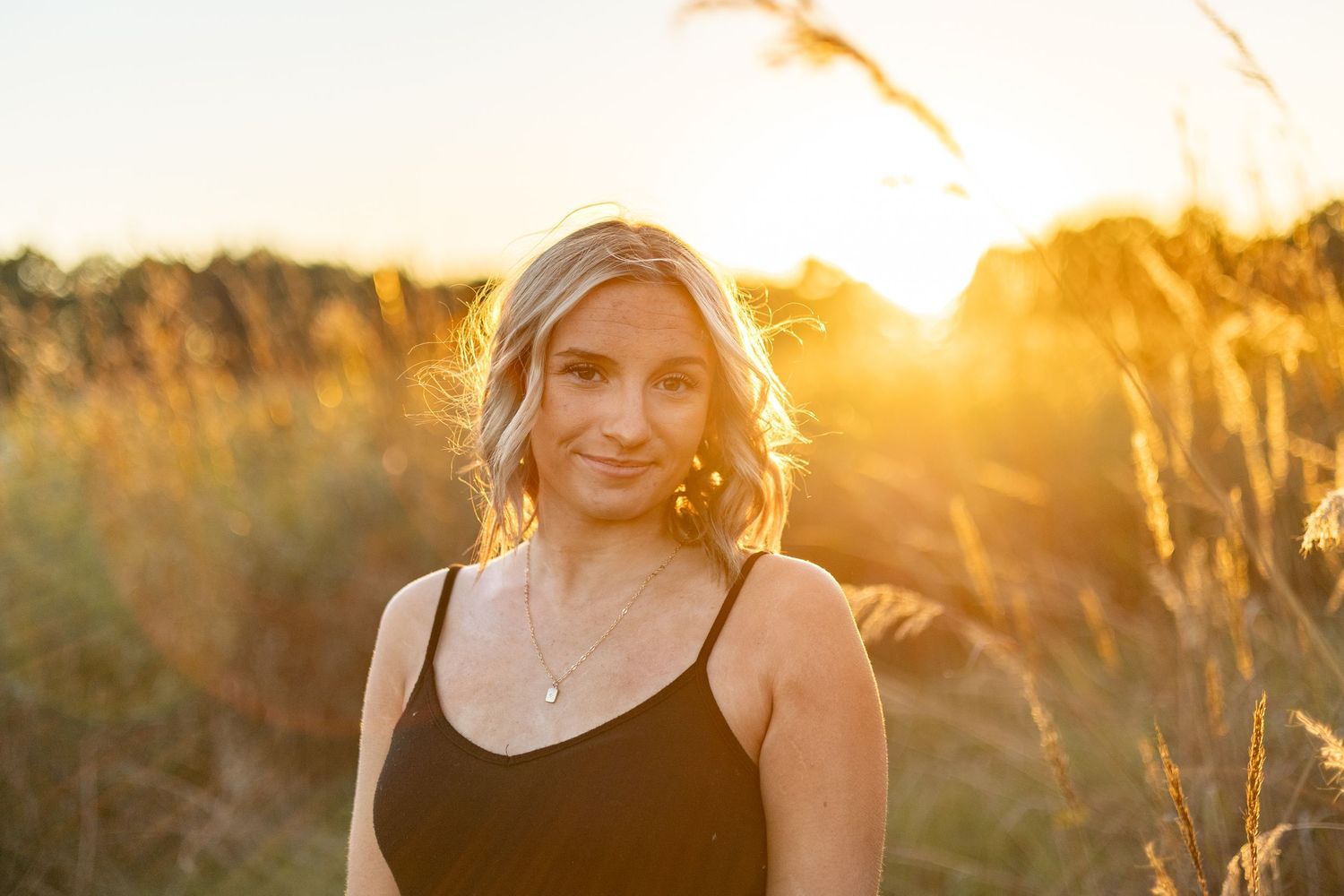 Woman in casual attire photographed during golden hour in field with backlit grass.