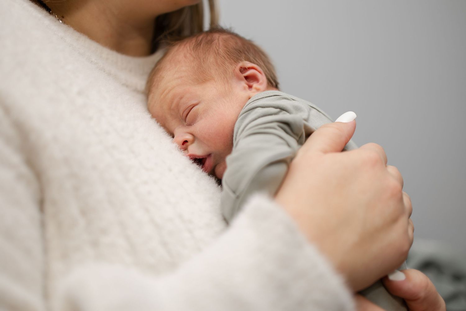 Sleeping newborn being held against soft white sweater.