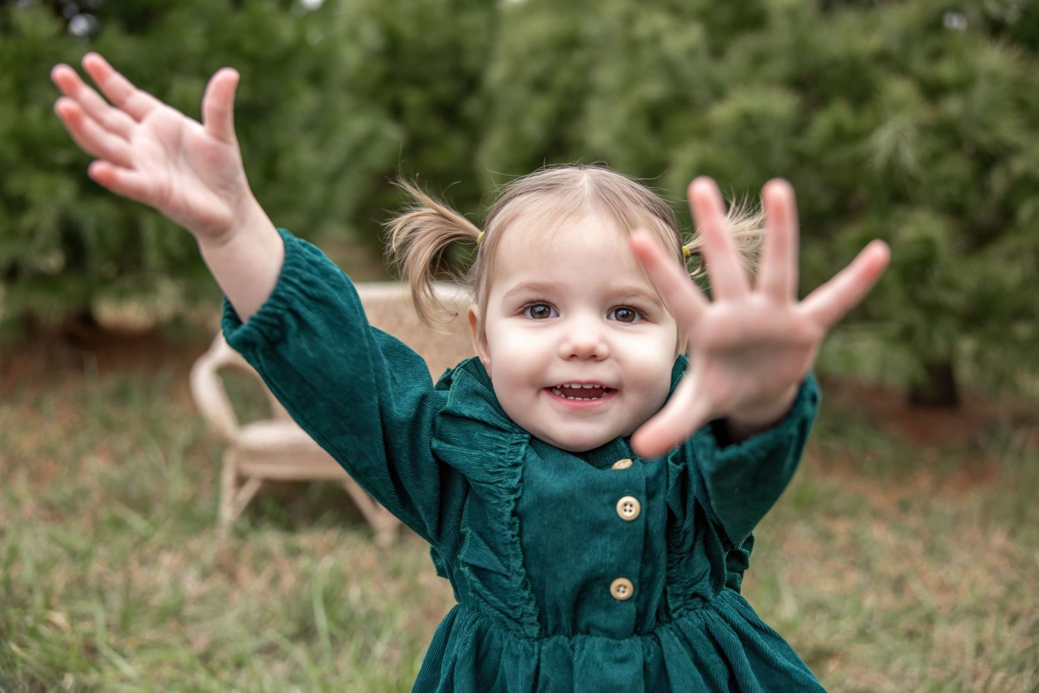 Small child in green dress raises arms with excited expression.