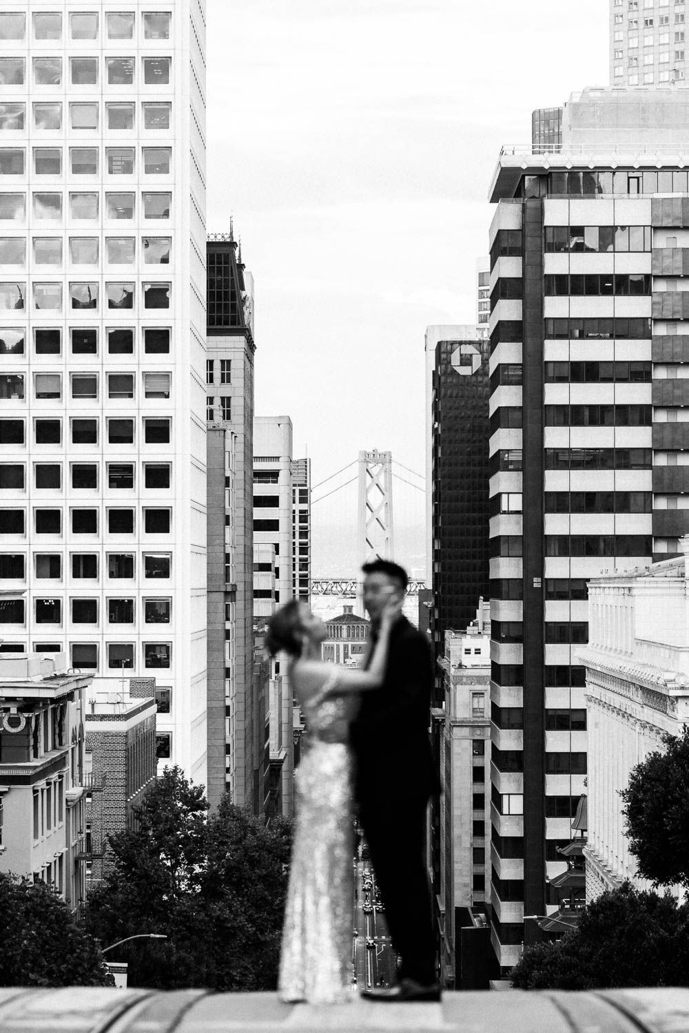 A black and white cityscape view of San Francisco with tall office buildings and a newly wedded couple standing on a hill.